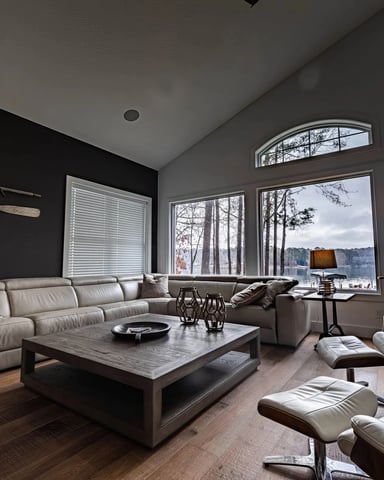Modern living room with gray sectional sofa, low coffee table, and large windows overlooking a lake with bare trees