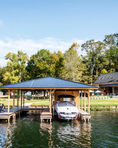 Waterfront property with boat dock, covered boathouse, and modern brick building with metal roof surrounded by mature trees
