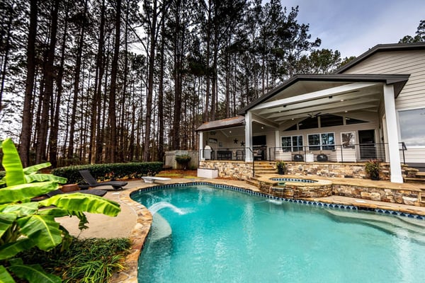 Modern house with covered porch and swimming pool surrounded by tall pine trees and tropical plants